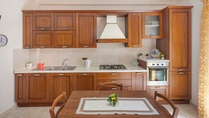 A kitchen with wooden cabinets, a stove, an oven, and a dining table with chairs.