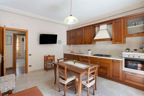 A kitchen with wooden cabinets, a dining table with chairs, a stove, and a television on the wall.