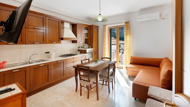 A kitchen with wooden cabinets, a dining table with chairs, a sofa, and a television.