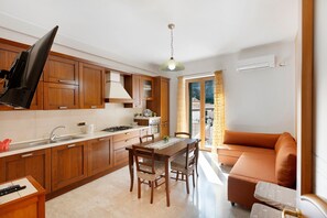 A kitchen with wooden cabinets, a dining table with chairs, a sofa, and a television. - Apartment 'Ce Tour - La Casa del Limone di Nonni' with Mountain View, Wi-Fi and Air Conditioning (Cetara)
