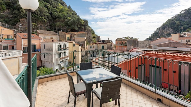A balcony with a table and chairs, a lamp, and a view of a hillside town. - Apartment 'Ce Tour - Casa Cetara Centro 1' with Private Terrace, Wi-Fi and Air Conditioning (Cetara)