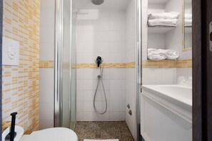 A shower with a glass door, a white sink with a mirror, and a towel rack with folded towels.