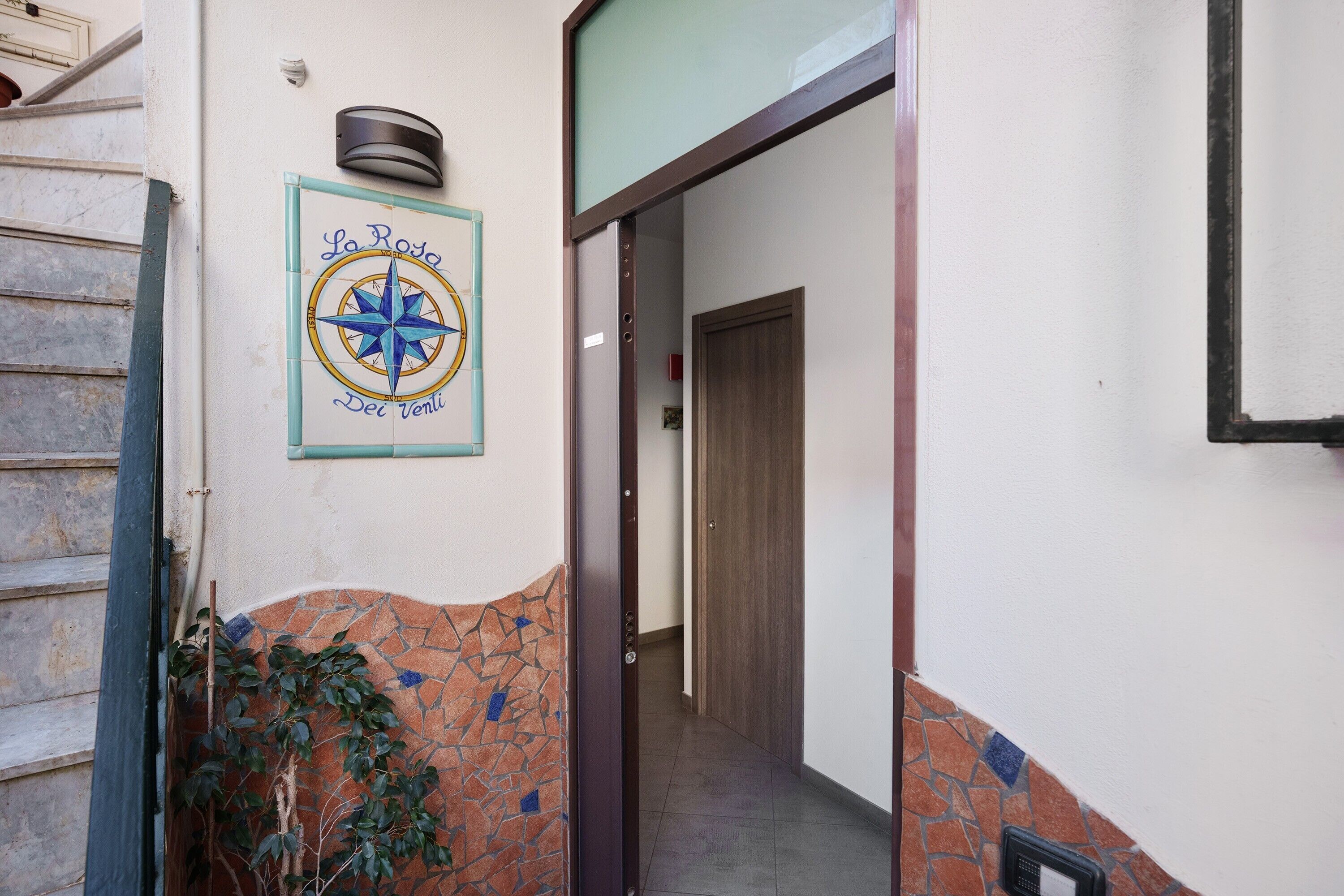 A hallway with a tiled wall, a wooden door, and a wall-mounted compass sign.