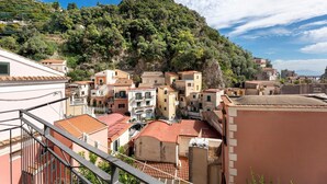 Un pueblo en la ladera de una colina con edificios de tejados de terracota, un balcón con barandilla metálica y cielo despejado.