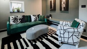 A living room with a green sofa, a patterned armchair, a black and white rug, and a window with a plant. - ‘Torri e Tramonti’ Apartment with Private Terrace and Air Conditioning (Albenga)