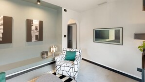 A hallway with a patterned armchair, wall-mounted artwork, and a potted plant. - ‘Torri e Tramonti’ Apartment with Private Terrace and Air Conditioning (Albenga)