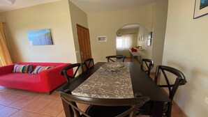 A dining area with a long table, six chairs, a red sofa with colorful cushions, and a painting on the wall. - Apartamentos Gran Rey Nº 8 (Valle Gran Rey)