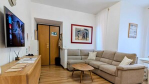 A modern living room with a wooden desk, a beige sofa, a small round table, a flat-screen TV, and a framed picture on the wall. - Family-friendly apartment. 20 min walk to Vatican and shoping areas. (Roma)