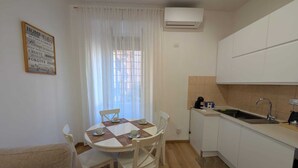 A compact kitchen with white cabinets, a dining table with chairs, a small sink, and an air conditioning unit. - Family-friendly apartment. 20 min walk to Vatican and shoping areas. (Roma)