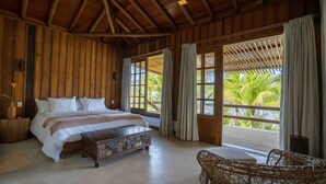 A wooden room with a bed, a small table, and a view of palm trees. - Fazenda Jeribucaçu (Itacaré)