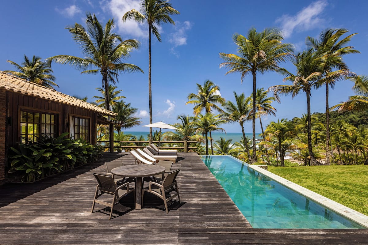 A wooden deck with a pool, lounge chairs, and a view of the ocean.