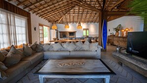A living room with a sofa, a coffee table, and a TV. There is a kitchen area in the background. - Fazenda Jeribucaçu (Itacaré)