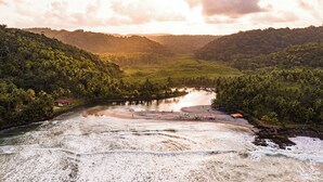 A river surrounded by lush greenery and hills. There are boats and a small dock with umbrellas. - Fazenda Jeribucaçu (Itacaré)