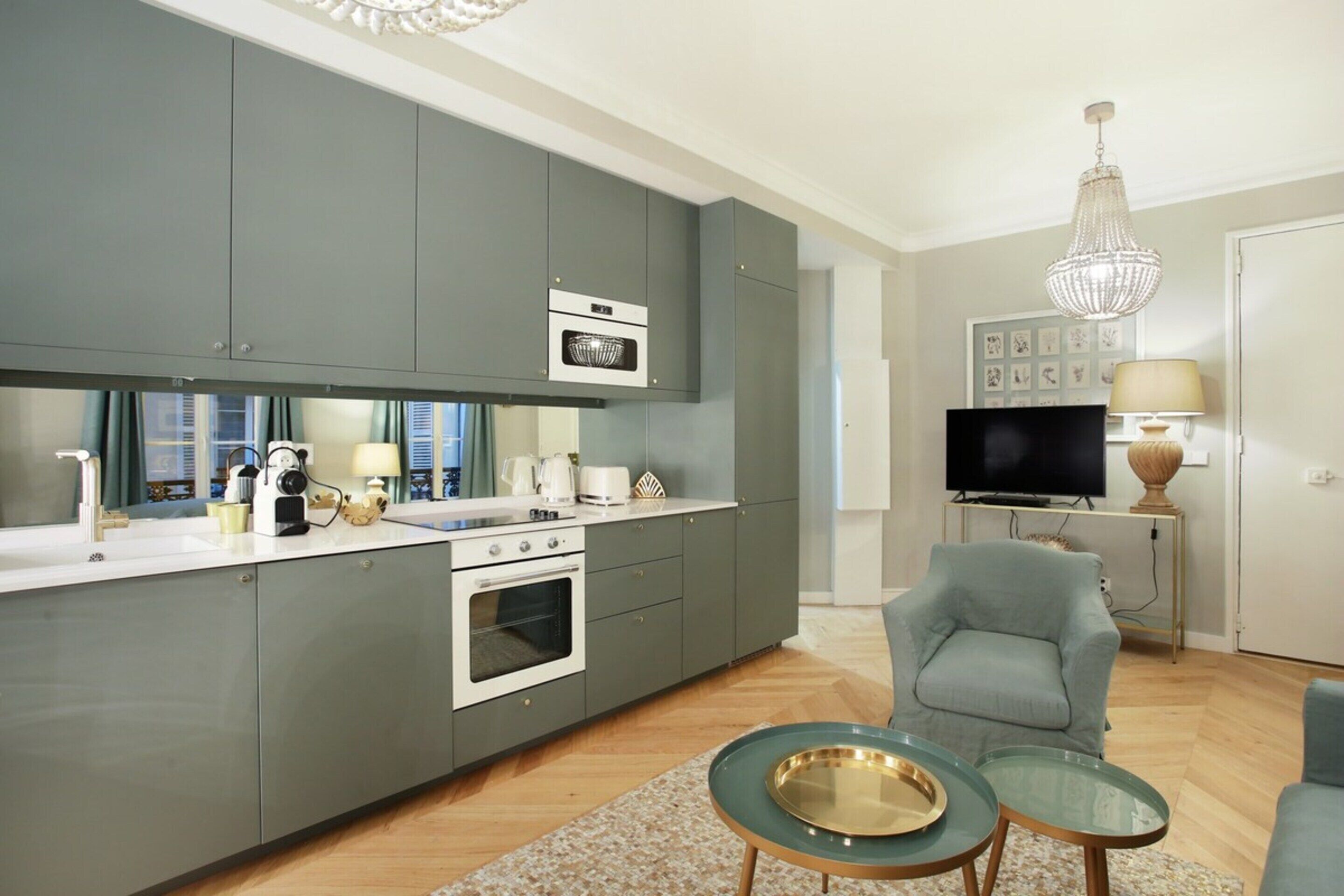 A modern kitchen with grey cabinets, a built-in oven, and a dining area with a glass table and chair.