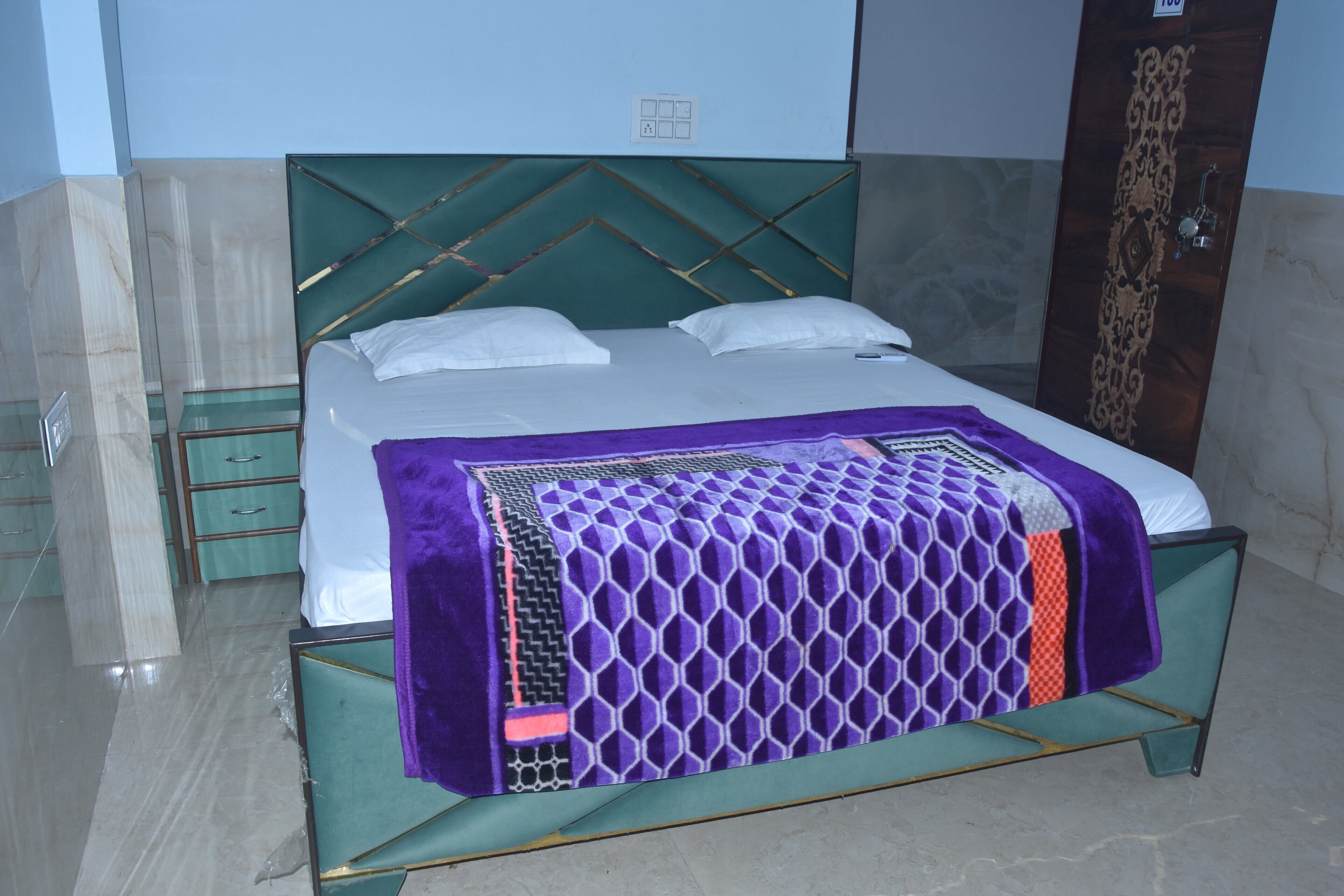 Een bed met een geometrisch hoofdbord, een paars beddegoed met een patroon en witte kussens.