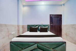 A bed with a green upholstered headboard, a dark wooden door, and light blue walls. - SKD  (Kanpur)