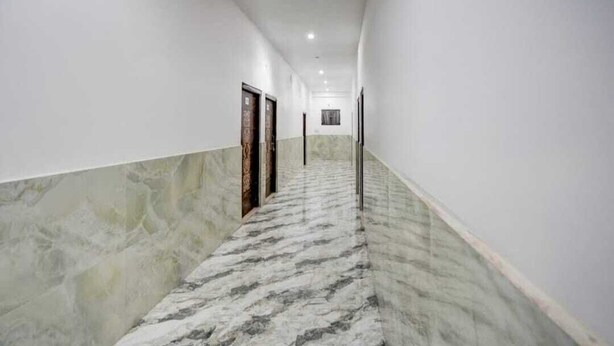 Un pasillo con suelo de mármol y paredes blancas, que conduce a una puerta al final.