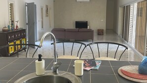 A kitchen with a sink, faucet, and a countertop. There is a refrigerator, a television, and a sofa in the background. - Luxury villa with private pool and staff close to the beach and Saly (N'Guerigne Bambara)