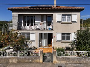 Un edifici de dues plantes amb un balcó, una escala i una entrada tancada per una reixa.