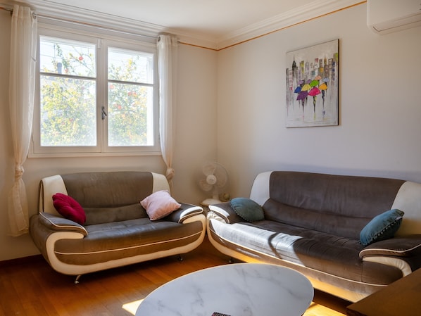 A living room with two sofas, a marble coffee table, a window with curtains, and a wall-mounted artwork.