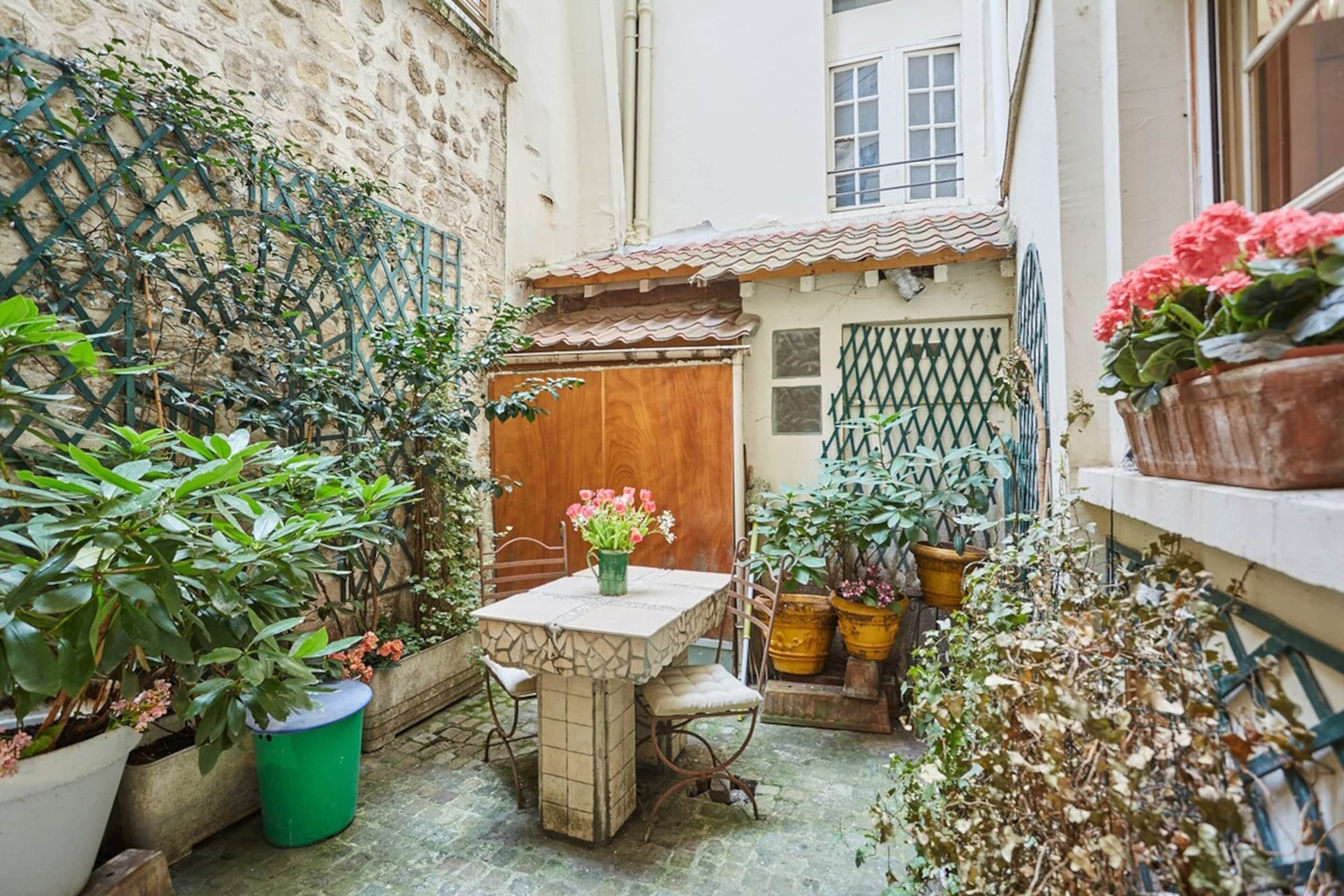 A courtyard with a stone table and chairs, surrounded by potted plants and a wooden door.