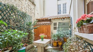 A courtyard with a stone table and chairs, surrounded by potted plants and a wooden door. - Superbe Apartment Le Marais/place des Vosges (Paris)