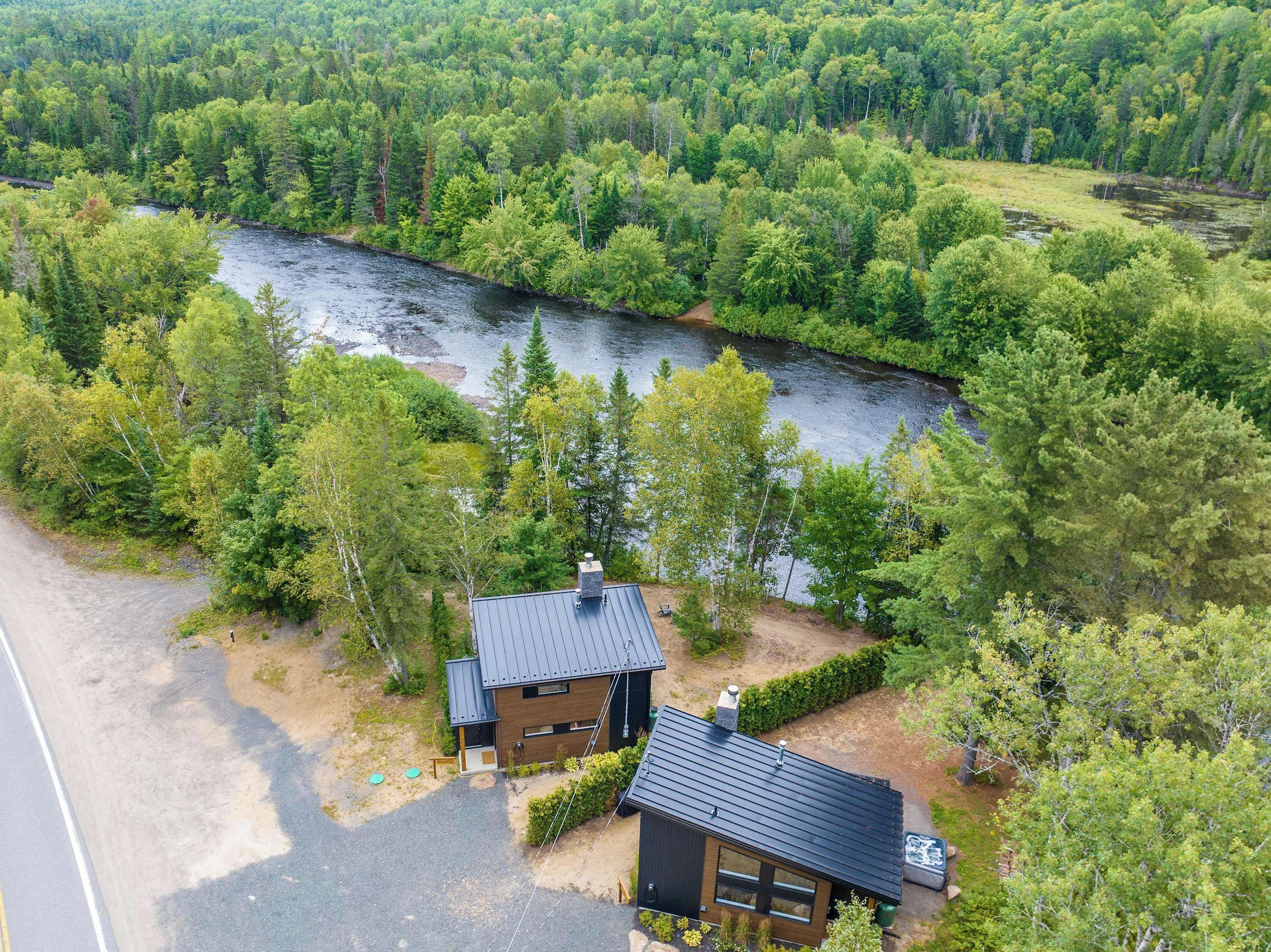 Ein modernes Haus mit dunklem Dach, umgeben von dichtem Wald und einem Fluss.