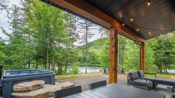 Ein Sitzbereich im Freien mit Whirlpool, Holzterrasse und Blick auf Wald und See.