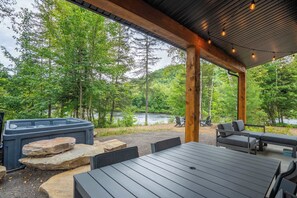 Ein Sitzbereich im Freien mit Whirlpool, Holzterrasse und Blick auf Wald und See.