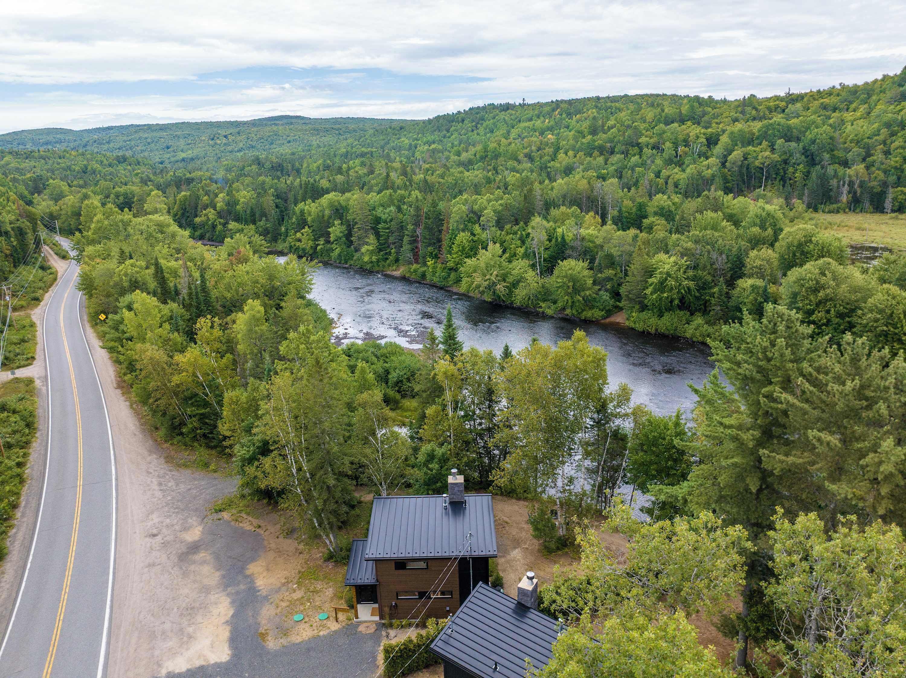 Talo, jonka katto on tehty metallista, ja jonka ympärillä on tiheä metsä sekä virtaava joki.