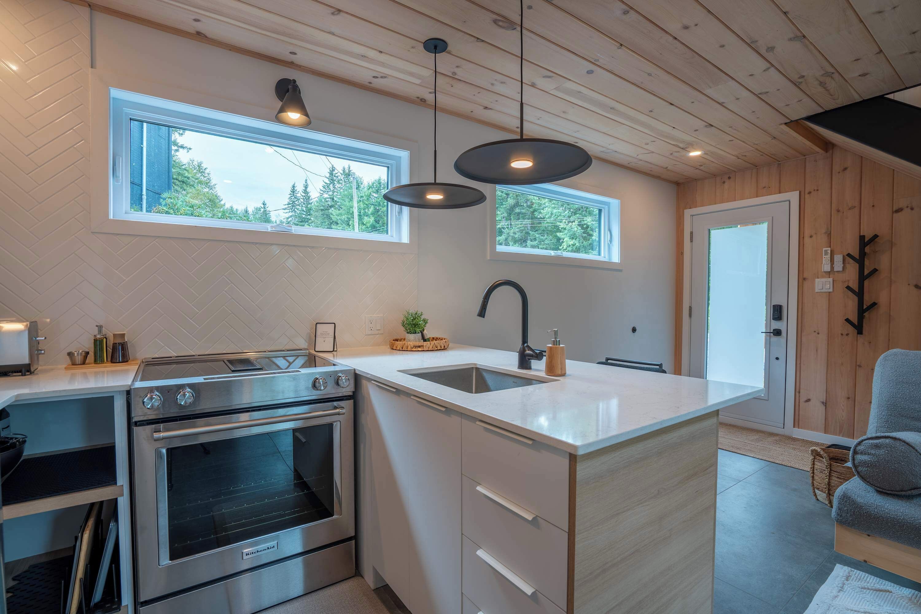 Une cuisine moderne dotée d’un four encastré, d’un évier et de luminaires suspendus.
