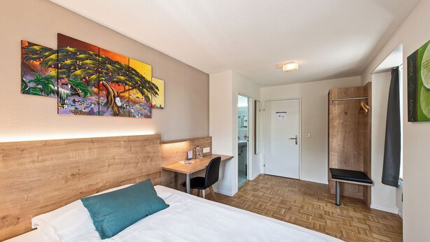 A hotel room with a bed, a desk, and a shower area. - Hotel zum Hirschen  (Schindellegi)