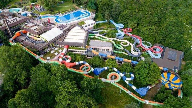 Une vue aérienne d’un parc aquatique doté de nombreux toboggans et de plusieurs piscines, le tout entouré d’une végétation luxuriante.