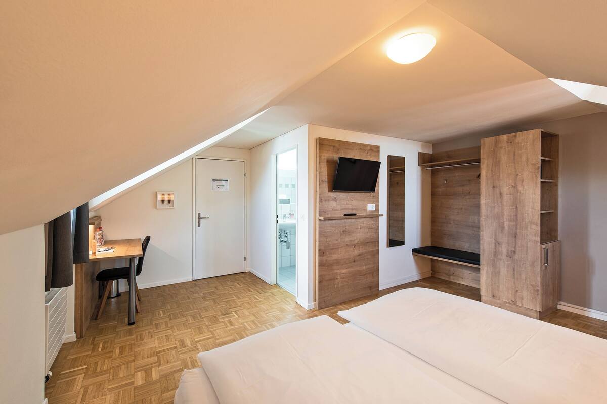 Une chambre avec un plancher en bois, un lit, un bureau avec une chaise, une armoire et un téléviseur fixé au mur.