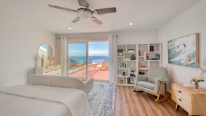 A bedroom with a bed, a chair, a desk, a bookshelf, and a view of the ocean. - @ Marbella Lane - Ocean Views & Heavenly Sunset (Pacifica)