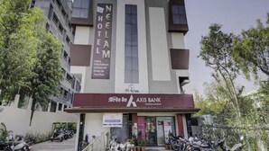 Um hotel com design moderno, exibindo uma placa chamativa do Neelam Hotel e uma agência do Axis Bank.