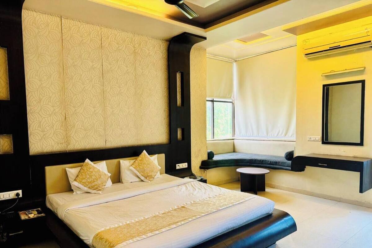 Ein modernes Hotelzimmer mit einem großen Bett, einer eingebauten Sitzbank, einem kleinen Tisch und einem großen Spiegel.