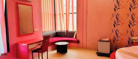 A room with a red and white color scheme, a bed, a desk with a chair, a small table, and a window with curtains.
