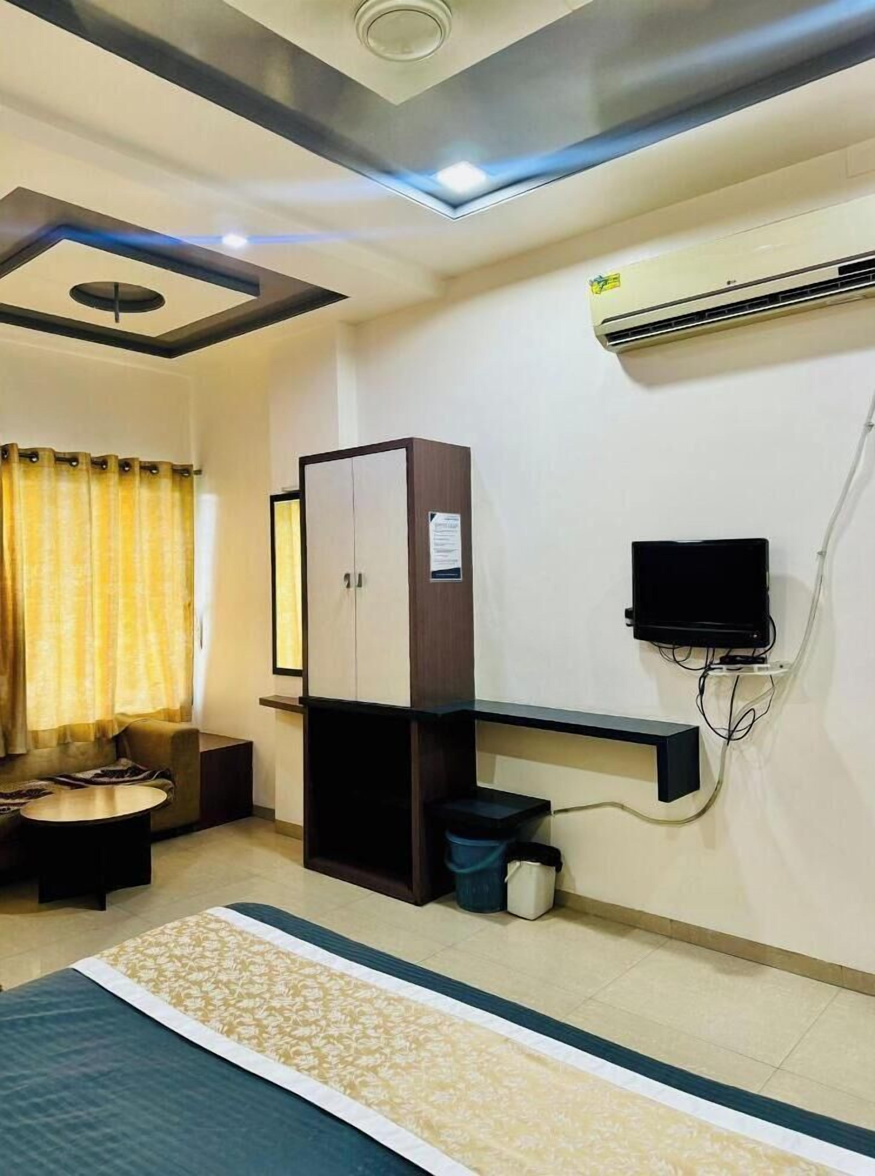 A hotel room with a bed, a sofa, a TV, an air conditioning unit, and a cabinet.
