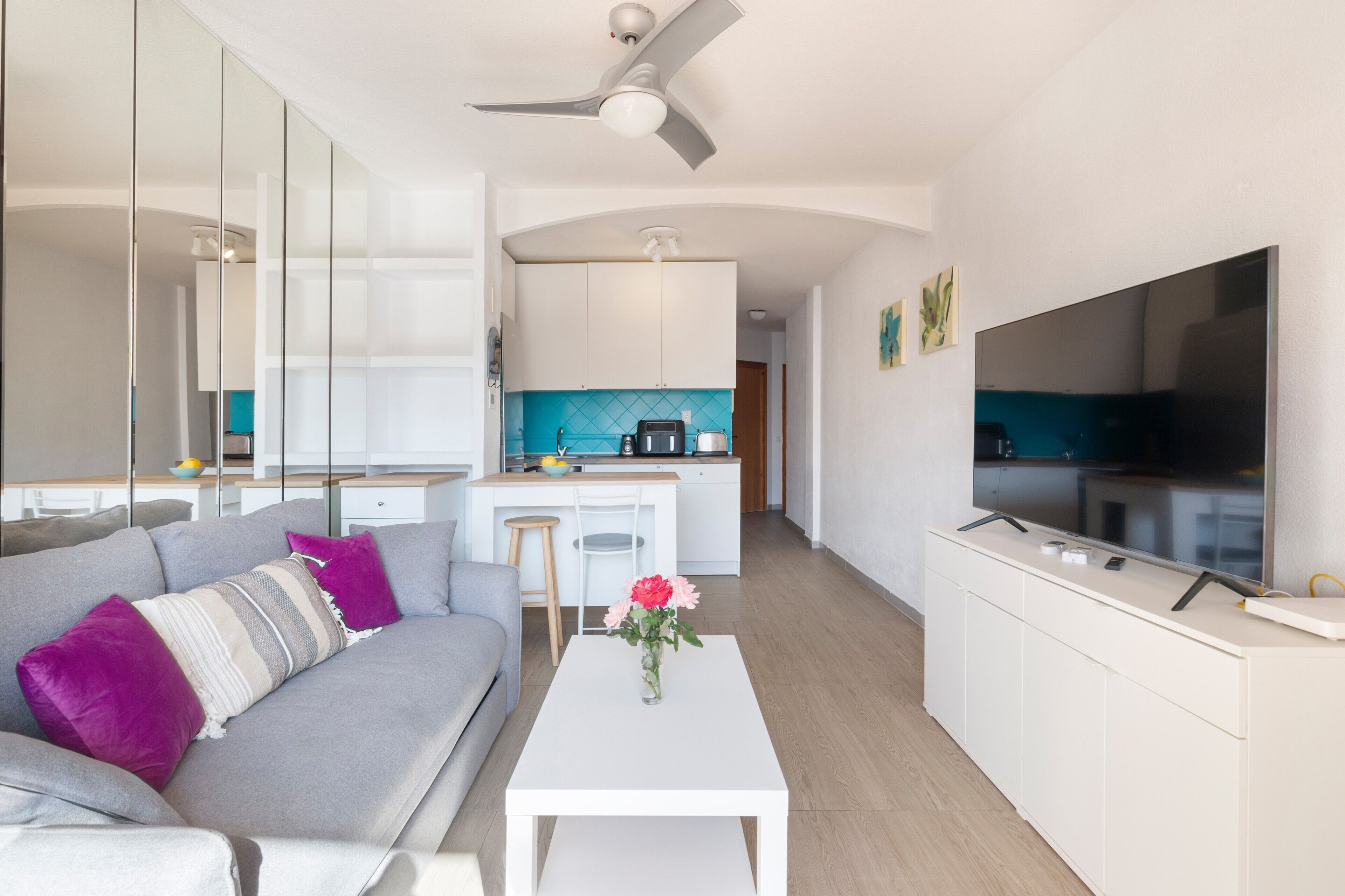 A modern living room with a sofa, a coffee table, a flat-screen TV, and a kitchen area in the background.
