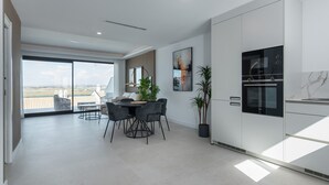 Una cocina moderna con armarios blancos, horno integrado y un comedor con mesa y sillas.