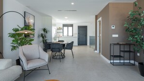 Una sala de estar moderna con comedor, una cocina al fondo y una planta grande en maceta.