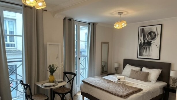 A bedroom with a bed, bedside table, chair, and a window with curtains. - Lovely Studio With AC - Center of Paris (Paris)