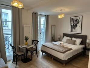 A bedroom with a bed, bedside table, chair, and a window with curtains. - Lovely Studio With AC - Center of Paris (Paris)