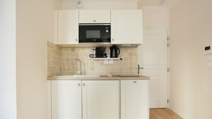 A compact kitchen with white cabinets, a black microwave, and a coffee maker on the countertop. - Lovely Studio With AC - Center of Paris (Paris)