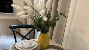 A dining table with a yellow vase of flowers, two plates, and two glasses. - Lovely Studio With AC - Center of Paris (Paris)