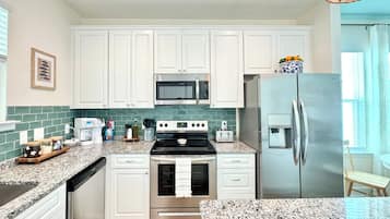 A modern kitchen with white cabinets, stainless steel appliances, a granite countertop, and a wooden floor.