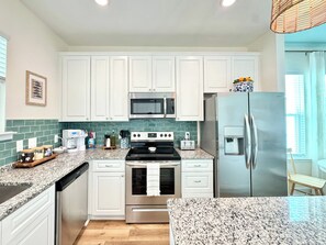 Una cocina moderna con armarios blancos, electrodomésticos de acero inoxidable, encimera de granito y piso de madera.