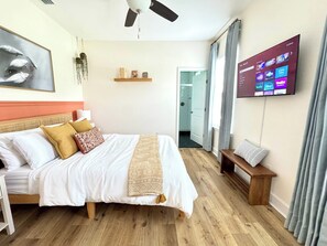 A bedroom with a bed, a TV mounted on the wall, a ceiling fan, and a wooden bench.