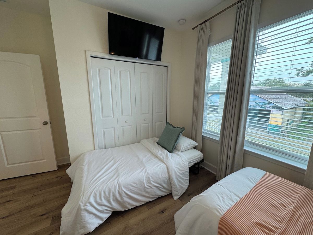 Une chambre avec deux lits, un téléviseur fixé au-dessus d’une armoire et une fenêtre avec des rideaux.